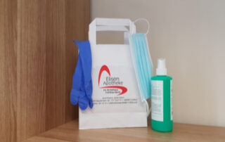 Das Bild zeigt eine Papiertüte von der Eisen Apotheke, die mit einer Gesichtsmaske, Einweghandschuhen und einem Fläschchen Desinfektionsmittel gefüllt ist. Es handelt sich offensichtlich um ein Hygiene-Set, das von der Apotheke zusammengestellt wurde, wahrscheinlich zur Prävention von Infektionen. Die Präsentation ist ordentlich und professionell, was auf einen Fokus auf Hygiene und Kundenservice hinweist. Das Bild vermittelt ein Gefühl von Sicherheit und Vorsorge in Zeiten von Pandemien oder erhöhter Infektionsgefahr. Die Farben sind dezent und beruhigend.